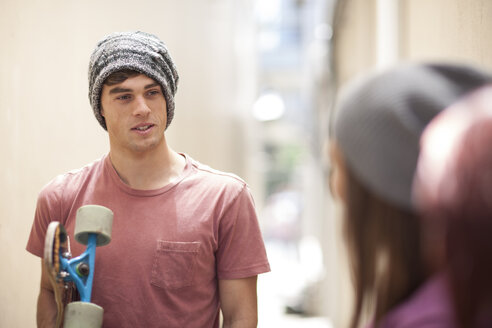 Young man with skateboard in a passageway talking to friends - ZEF007580