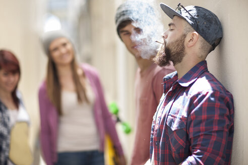 Young man smoking a cigarette with friends in background - ZEF007582