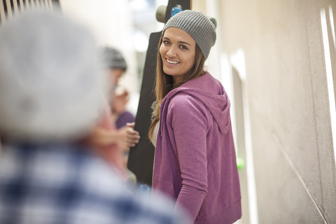 Lächelnde junge Frau mit Skateboard in einer Passage, lizenzfreies Stockfoto