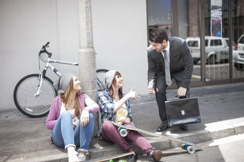 Businessman giving a lighter to two female friends on city street - ZEF007594