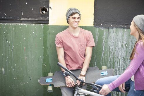 Young man with skateboard smiling at teenage girl - ZEF007595