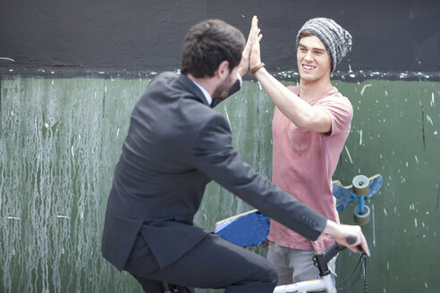 Young man with skateboard high fiving with businessman on bicycle - ZEF007601