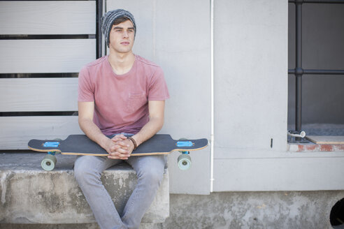 Young man with skateboard sitting outdoors - ZEF007602