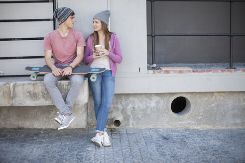 Young man with skateboard and teenage girl sitting outdoors - ZEF007603