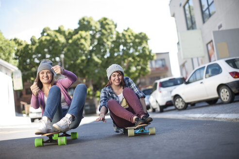 Zwei Freunde sitzen auf Skateboards und fahren die Straße entlang - ZEF007616