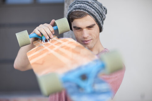 Young man scrutinizing his skateboard - ZEF007617