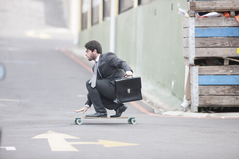 Businessman riding on skateboard - ZEF007623