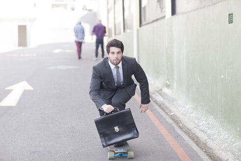 Businessman on skateboard riding down the street - ZEF007624