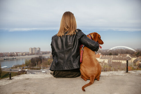 Serbien, Novi Sad, Rückenansicht einer jungen Frau, die neben ihrem Hund sitzt und die Aussicht betrachtet - ZEDF000033