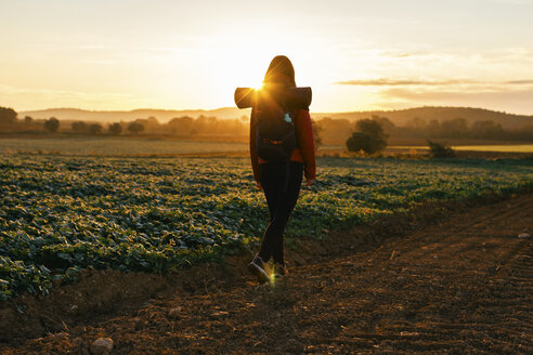 Spain, Catalunya, Girona, woman hiking on field path at sunrise - EBSF001179
