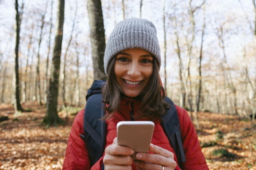 Spanien, Katalonien, Girona, Porträt einer lächelnden Wanderin im Wald mit Mobiltelefon - EBSF001199