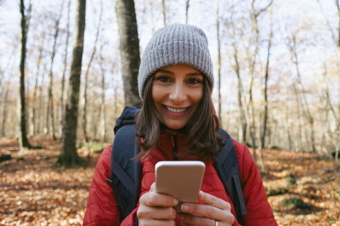 Spain, Catalunya, Girona, portrait of smiling female hiker in the woods with cell phone - EBSF001199