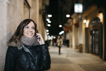 Spain, Reus, portrait of smiling young woman telephoning with smartphone at night - JRFF000249