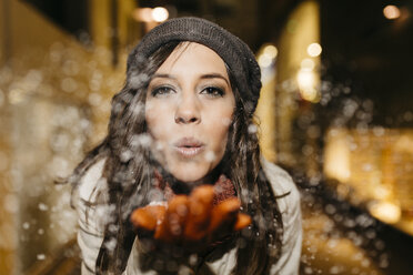 Spain, Reus, portrait of young woman blowing snow in the air at night - JRFF000252