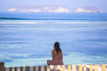 Indonesien, Sumbawa, junge Frau sitzt am Strand und schaut aufs Meer - KNTF000219