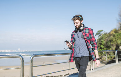 Spanien, La Coruna, Hipster mit Kopfhörern schaut auf sein Smartphone - RAEF000722