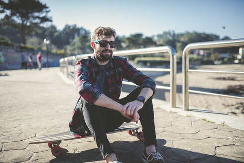 Spanien, La Coruna, Porträt eines Hipsters mit Sonnenbrille, der auf seinem Longboard sitzt - RAEF000733