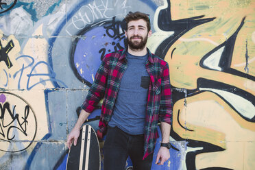 Spain, La Coruna, portrait of hipster leaning against wall with his longboard - RAE000737