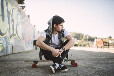 Spain, La Coruna, young man sitting on his longboard - RAEF000742