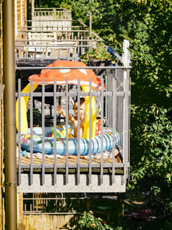 Kleines Mädchen planscht im Planschbecken auf dem Balkon an einem Sommertag - KRPF001686