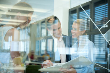 Smiling business team behind glass wall in office looking at folder - WESTF021630