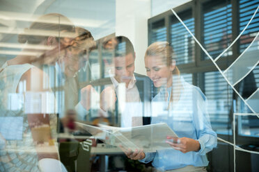 Successful business team behind glass wall in office looking at folder - WESTF021631
