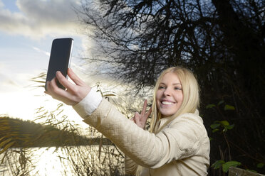 Porträt einer lächelnden blonden Frau, die ein Selfie mit Smartphone in der Natur macht - BFRF001703