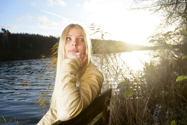 Portrait of pensive blond woman sitting in front of a lake - BFRF001705