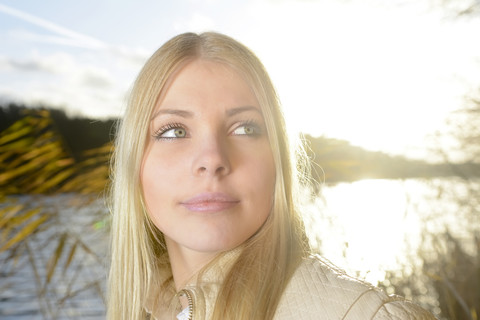 Porträt einer blonden Frau vor einem See bei Gegenlicht, lizenzfreies Stockfoto