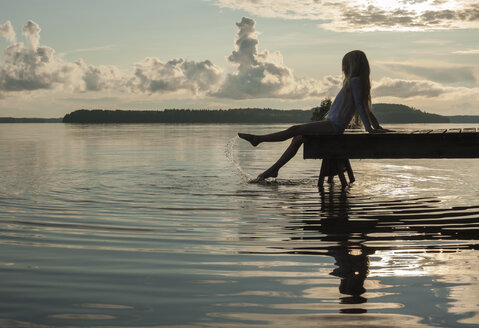 Finnland, Karelien, Uukuniemi, Pyhäjärvi-See, Mädchen sitzt auf Steg und planscht mit den Füßen im Wasser - JBF000263