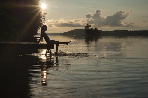 Finnland, Karelien, Uukuniemi, Pyhäjärvi-See, Mädchen sitzt auf Steg und planscht mit den Füßen im Wasser - JBF000264