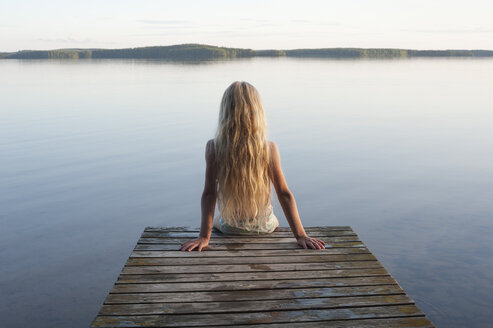 Finnland, Karelien, Uukuniemi, Pyhäjärvi-See, Rückenansicht eines auf dem Steg sitzenden Mädchens - JBF000265