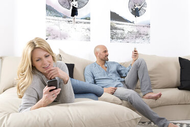 Mature couple sitting on sofa using their smart phones - MAEF011073