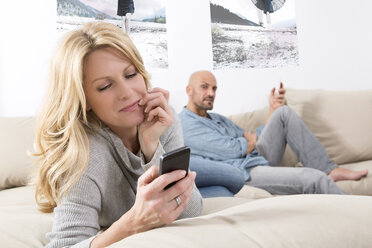 Mature couple sitting on sofa using their smart phones - MAEF011074
