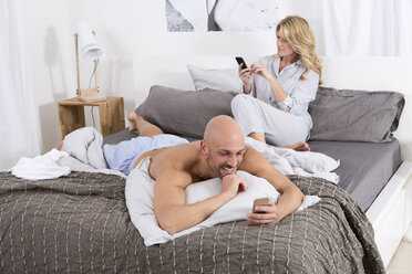 Reifes Paar im Schlafzimmer, das seine Handys benutzt - MAEF011076