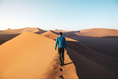 Namibia, Namib-Wüste, Sossusvlei, Mann geht auf dem Gipfel der berühmten Düne 45 bei Sonnenaufgang - GEMF000555