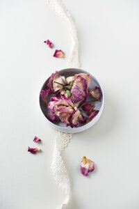 Schale mit getrockneten Rosenblüten und Spitze auf weißem Grund - MYF001273
