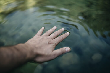 Die Hand eines Mannes berührt die Wasseroberfläche eines Bergsees - JRFF000259