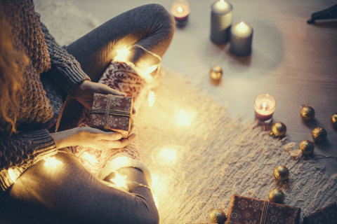 Woman sitting with Christmas present and fairy lights on the carpet stock photo