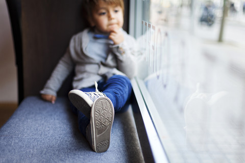 Kleiner Junge sitzt auf dem Fensterbrett, lizenzfreies Stockfoto