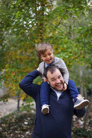 Lachender kleiner Junge, der auf den Schultern seines Vaters sitzt, lizenzfreies Stockfoto