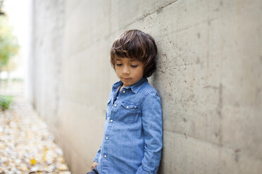 Porträt eines traurigen kleinen Jungen mit Jeanshemd, der an einer Betonwand lehnt - VABF000022