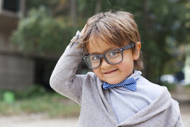Porträt eines lächelnden kleinen Jungen mit Hand auf dem Kopf, der eine Fliege und eine übergroße Brille trägt - VABF000026