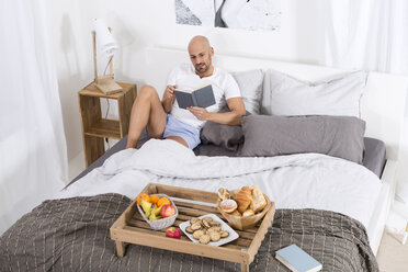 Reifer Mann mit Büchern und Frühstück im Bett - MAEF011117