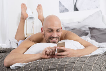 Mature man using smartphone lying on bed - MAEF011119