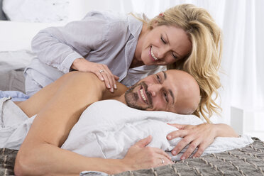Glückliches Paar im Schlafzimmer, Frau gibt Mann eine Rückenmassage - MAEF011126