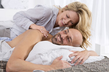 Happy couple in bedroom, woman giving man a back massage - MAEF011126