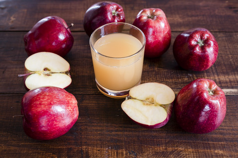 Ganze und geschnittene rote Äpfel und ein Glas Apfelsaft auf Holz, lizenzfreies Stockfoto