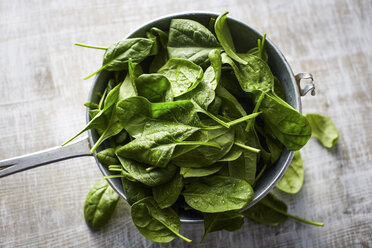 Fresh spinach leaves in colander on wood - KSWF001718