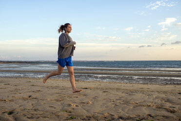 Spanien, Puerto Real, junge Frau beim Joggen am Strand in der Abenddämmerung - KIJF000042